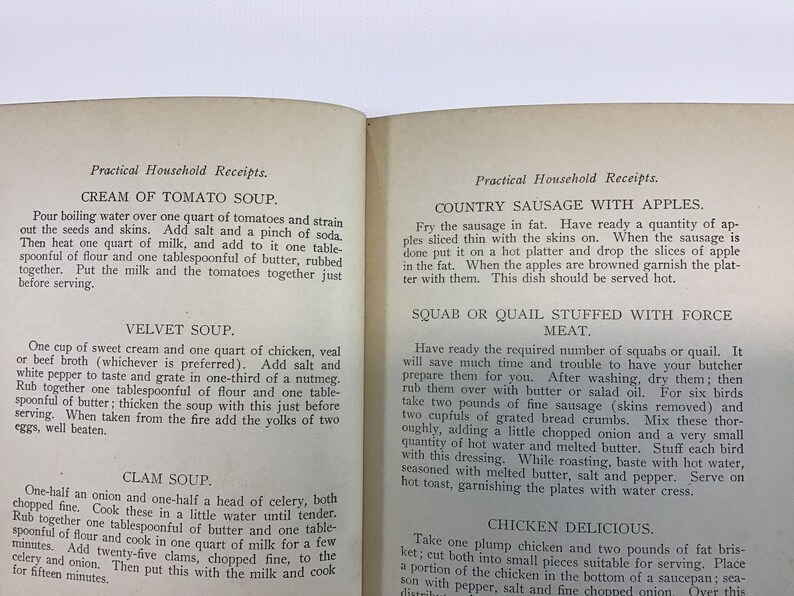 May include: A vintage cookbook with a yellowed, cream-colored cover and black text. The title of the book is "Practical Household Receipts." The book contains recipes for Cream of Tomato Soup, Velvet Soup, Clam Soup, Country Sausage with Apples, and Squab or Quail Stuffed with Force Meat.