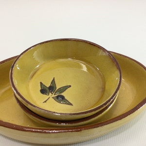May include: A set of three yellow ceramic bowls with brown rims. The smallest bowl has a green olive branch design.