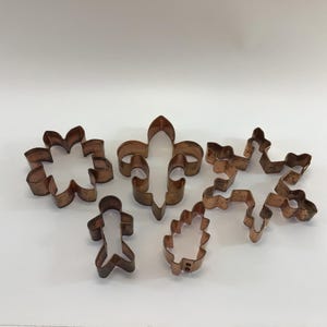 Könnte beinhalten: Satz von sechs antiken Keksausstechern aus Kupfer, darunter eine Fleur-de-lis, eine Schneeflocke, eine Blume, ein Blatt und zwei Personenformen.