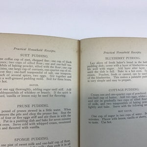 May include: An open vintage cookbook with recipes for Suet Pudding, Blueberry Pudding, Cottage Pudding, Prune Pudding, and Sponge Pudding. The book has a yellowed, cream-colored paper cover with black text.
