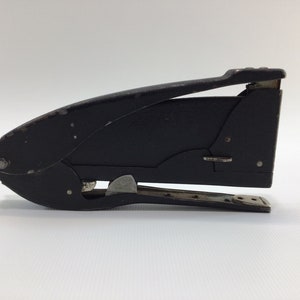 May include: A black metal stapler with a silver lever and a silver base. The stapler is closed and ready to use.
