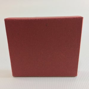 K&ouml;nnte beinhalten: Eine kleine, rechteckige Schachtel aus rotem Karton. Die Schachtel ist leer und hat eine glatte Oberfl&auml;che.