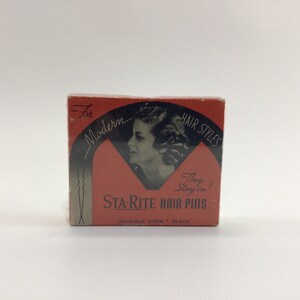 May include: A red box with black text that reads "For Modern Hair Styles" and "STA-RITE HAIR PINS". The box features a black and white image of a woman with short, wavy hair. The text "They Stay in!" is also on the box.