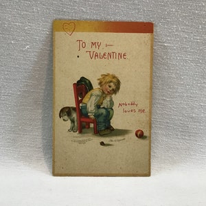 May include: Vintage Valentine's Day card featuring a cartoon illustration of a sad boy sitting on a red chair with a dog beside him. The card reads "To my Valentine. Nobody loves me."