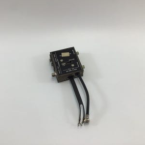 May include: A black antenna signal splitter with multiple inputs and outputs. The device has a switch and is labeled with text including "TO TV" and "ANTENNA". Two black cables extend from the bottom.