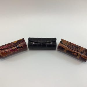 May include: Three small, rectangular leather cases. One is black with a crocodile pattern, one is brown with a floral pattern, and one is brown with a geometric pattern.