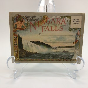 Könnte beinhalten: Vintage-Postkarte mit einer malerischen Ansicht der Niagarafälle mit einem Boot im Vordergrund. Die Postkarte hat einen dekorativen Rand mit indianischen Motiven und dem Text "Souvenir Folder of Niagara Falls".