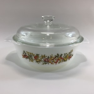 May include: White casserole dish with a clear glass lid. The dish features a colorful floral and vegetable design around the rim. The lid has a small knob for easy handling. A classic kitchenware item.