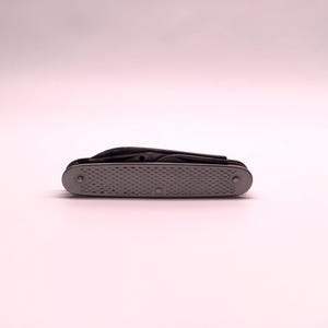 May include: A closed, silver pocket knife with a textured handle and several visible blades. The knife is set against a soft, white background.