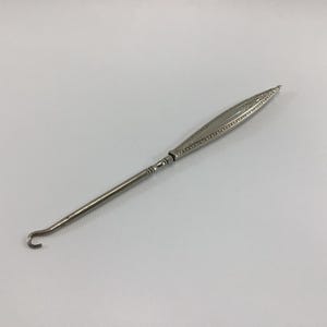 May include: A silver shoe horn with a decorative handle. The handle is engraved with a floral design.