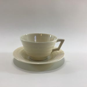 May include: A white teacup and saucer set with a ridged design. The cup has a rounded shape and a handle.