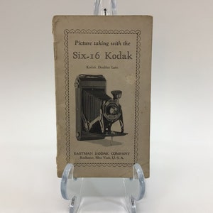 May include: A vintage instruction booklet for the Six-16 Kodak camera with a Kodak Doubler Lens. The booklet features a black and white illustration of the camera on the front cover. The text on the cover reads "Picture taking with the Six-16 Kodak" and "Kodak Doubler Lens". The bottom of the cover reads "Eastman Kodak Company Rochester, New York, U.S.A."