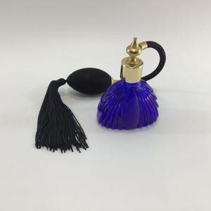 May include: A vintage cobalt blue perfume bottle with a gold-colored top and a black bulb atomizer. The bottle has a ribbed design and is paired with a black tassel. The atomizer has a black rubber tube.