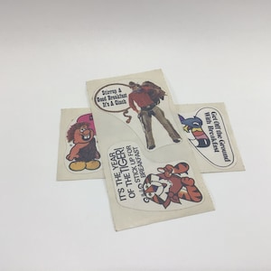 May include: Four vintage stickers featuring cartoon characters and slogans related to breakfast. The stickers are on a white background. The slogans include "Stirrup A Good Breakfast It's A Cinch", "It's The Year Of The Tiger! Stick Up For Breakfast", and "Get Off The Ground With Breakfast".