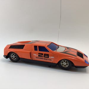May include: Orange and black remote-controlled toy car with the number 28 on the side. The toy car has a black stripe design on the hood and the words "Mercedes Benz C111" printed on the side.