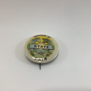 May include: A white and yellow round pin with the text "Souvenir of State Fair" and images of a horse, cow, and people riding horses.