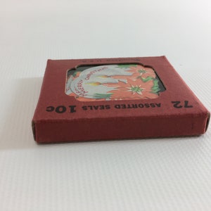 K&ouml;nnte beinhalten: Eine rote Schachtel mit dem Text "ASSORTED SEALS 10C" und "12" darauf gedruckt. Die Schachtel enth&auml;lt einen Satz von 12 runden Weihnachtssiegeln mit Bildern von Weihnachtssternen und Kerzen.