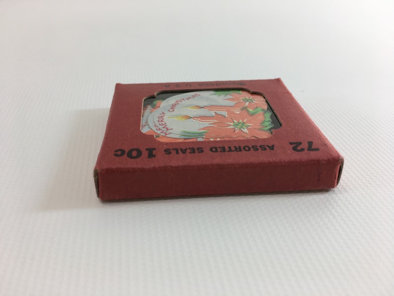 K&ouml;nnte beinhalten: Eine rote Schachtel mit dem Text "ASSORTED SEALS 10C" und "12" darauf gedruckt. Die Schachtel enth&auml;lt einen Satz von 12 runden Weihnachtssiegeln mit Bildern von Weihnachtssternen und Kerzen.