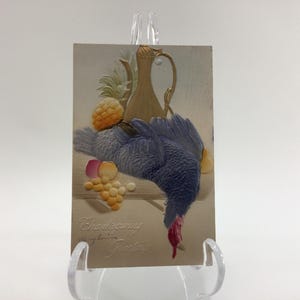 May include: A vintage Thanksgiving greeting card with a blue and purple turkey, a gold pitcher, and fruit. The card reads "Thanksgiving Greetings".