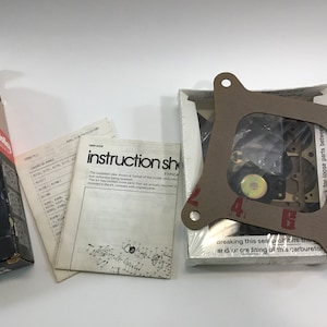 May include: A brown cardboard box with a white label that says "Holley Carburetor Kit". The box contains a carburetor kit with instructions and parts. The kit includes a gasket, a carburetor, and other parts.