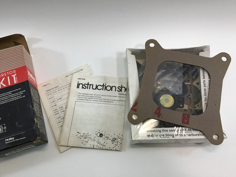 May include: A brown cardboard box with a white label that says "Holley Carburetor Kit". The box contains a carburetor kit with instructions and parts. The kit includes a gasket, a carburetor, and other parts.