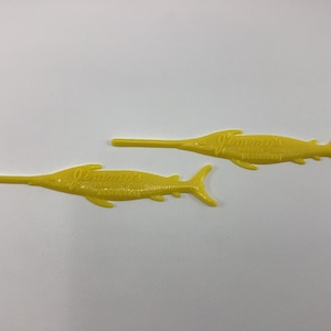 May include: Two yellow plastic fish-shaped cocktail picks with the text "Jimmy's Seafood Restaurant" printed on them.