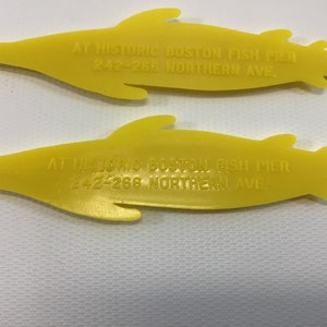 May include: Two yellow plastic fish-shaped promotional items with the text "AT HISTORIC BOSTON FISH PIER 242-266 NORTHERN AVE" printed on them.
