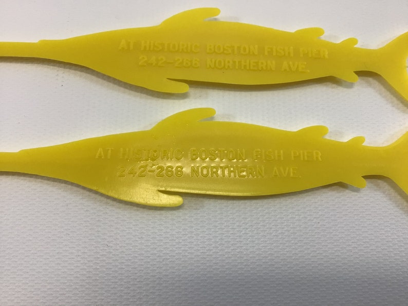 May include: Two yellow plastic fish-shaped promotional items with the text "AT HISTORIC BOSTON FISH PIER 242-266 NORTHERN AVE" printed on them.