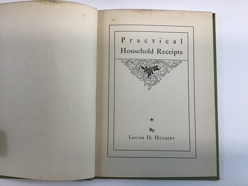 May include: A vintage book titled "Practical Household Receipts" by Louise D. Hulbert. The cover is a light green color with a white page showing a decorative title page with a floral design.