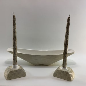 May include: A set of two white ceramic candle holders with a white ceramic bowl. The candle holders are shaped like tree trunks and the bowl is oval shaped.