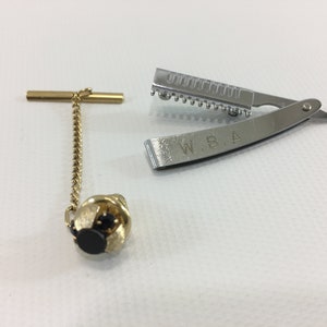 May include: A gold tie tack with a black stone and a silver straight razor with the inscription "W.B.A."