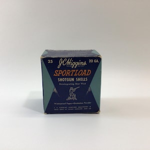 May include: A vintage J.C. Higgins Sportload shotgun shells box. The box is dark blue and teal with white lettering and a graphic of a person shooting a shotgun. The box reads "20 GA." and contains 25 shells.