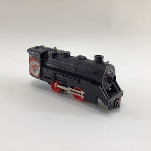 May include: A black toy train engine with red wheels and a Santa Claus design on the side.