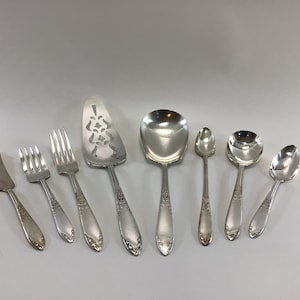 May include: A set of eight silver-plated serving utensils, including a butter knife, two forks, a cake server, a serving spoon, and three spoons.