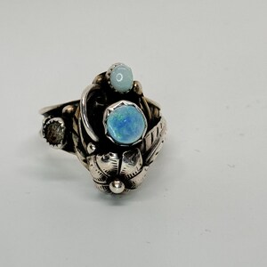 May include: A silver ring with a blue opal and a smaller blue stone set in a floral design.