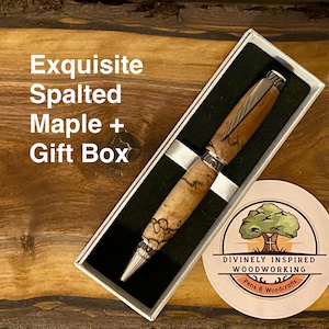 May include: An exquisite spalted maple pen in a gift box. The pen features a light brown and cream-colored wood grain with silver accents. The pen is presented in a white box with a black interior, and a round sticker with a tree logo.