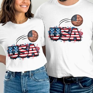 Two people wear white t-shirts featuring "USA" text and an American flag-themed basketball.