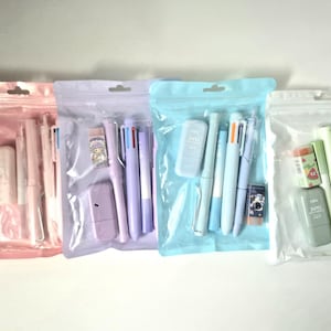 May include: Four clear plastic bags filled with stationery items. Each bag contains pens, erasers, and other supplies in shades of pink, purple, blue, and green. The bags are sealed and ready for use.