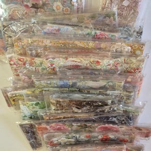 Könnte beinhalten: Ein Stapel einzeln verpackter dekorativer Papierbögen mit floralen und botanischen Designs. Die Papiere weisen verschiedene Farben auf, darunter Rosa, Gelb und Grün, und sind in klarem Kunststoff versiegelt.