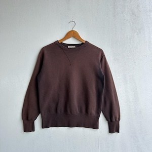May include: A brown crew neck sweatshirt with long sleeves, hanging on a wooden hanger. The sweatshirt has a ribbed hem and cuffs. The neckline features a small, stitched detail.