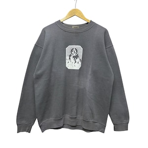 May include: Gray sweatshirt with a white graphic on the front. The graphic is a rectangular design with a mountain scene and the Volcom logo. The sweatshirt has a crew neck and long sleeves. The garment is hanging on a wooden hanger.
