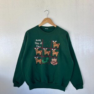 Könnte beinhalten: Ein dunkelgrünes Sweatshirt mit einem weihnachtlichen Design. Das Design umfasst gestickte Rentiere, einen Schlitten und den Text "away they all flew". Das Sweatshirt hat einen Rundhalsausschnitt und lange Ärmel.
