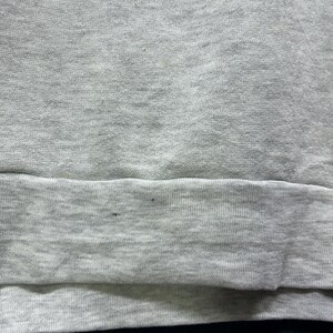 K&ouml;nnte beinhalten: Ein graues Sweatshirt mit blauem Text oben. Der untere Teil des Sweatshirts ist schwarz. Das Sweatshirt hat einen gerippten Saum. Der Stoff scheint ein weiches, bequemes Material zu sein.