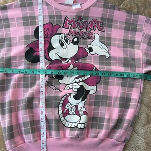 May include: Pink plaid Minnie Mouse sweatshirt with a graphic of Minnie Mouse. The sweatshirt has a crew neck and a pink ribbed hem and cuffs. The length is approximately 28 inches.
