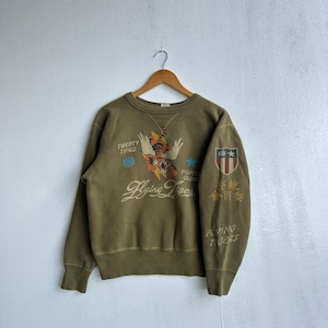 Può includere: Felpa verde oliva con grafica "Flying Tigers". Presenta un'illustrazione di tigre e testo, tra cui "Twenty Third" e caratteri giapponesi. Il top girocollo in stile vintage ha un aspetto invecchiato ed è appeso a una gruccia di legno.