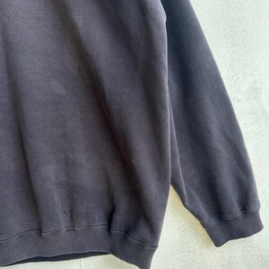 May include: A dark grey sweatshirt with ribbed cuffs and hem. The fabric has a soft, worn appearance. The image is a close-up of the garment, showing its texture and design details.