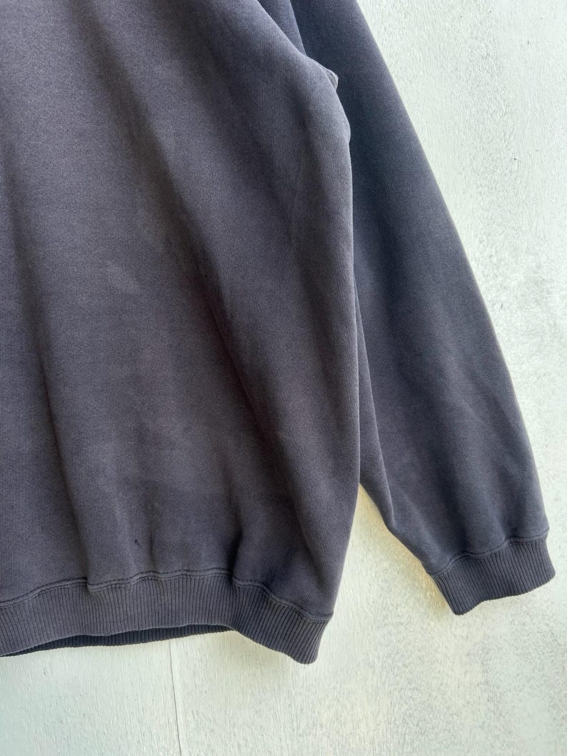 May include: A dark grey sweatshirt with ribbed cuffs and hem. The fabric has a soft, worn appearance. The image is a close-up of the garment, showing its texture and design details.