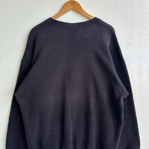 May include: A black crew neck sweatshirt hanging on a wooden hanger. The sweatshirt is a solid black colour and appears to be made of a soft, comfortable material. The garment has a classic, casual style.
