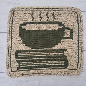 Può includere: Un sottopentola quadrato all'uncinetto con un disegno di tazza di caffè verde scuro su sfondo beige. La tazza è appoggiata su una pila di libri, con vapore che sale dalla tazza. Il sottopentola ha un bordo strutturato.