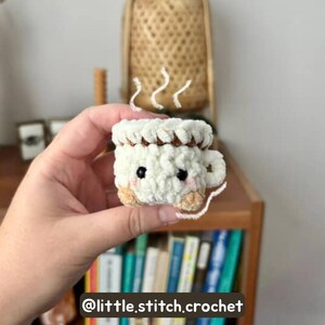 May include: A handmade, crocheted mug with a cute face and steam rising from the top. The mug is white with a brown rim and tan accents. The text "@little.stitch.crochet" is at the bottom of the image.